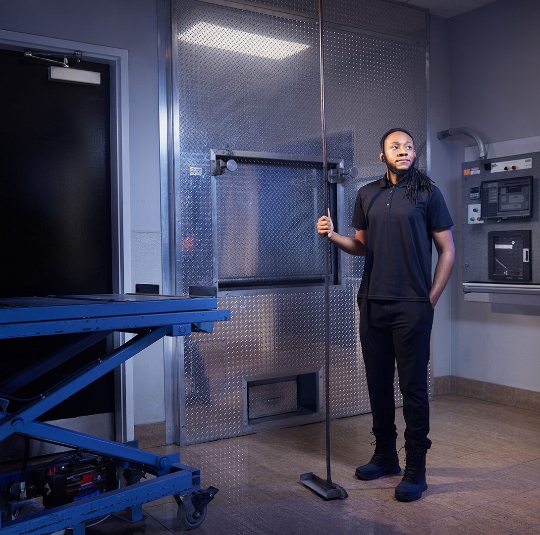 Crematorium technician standing in front of a cremation furnace in a preparation room.